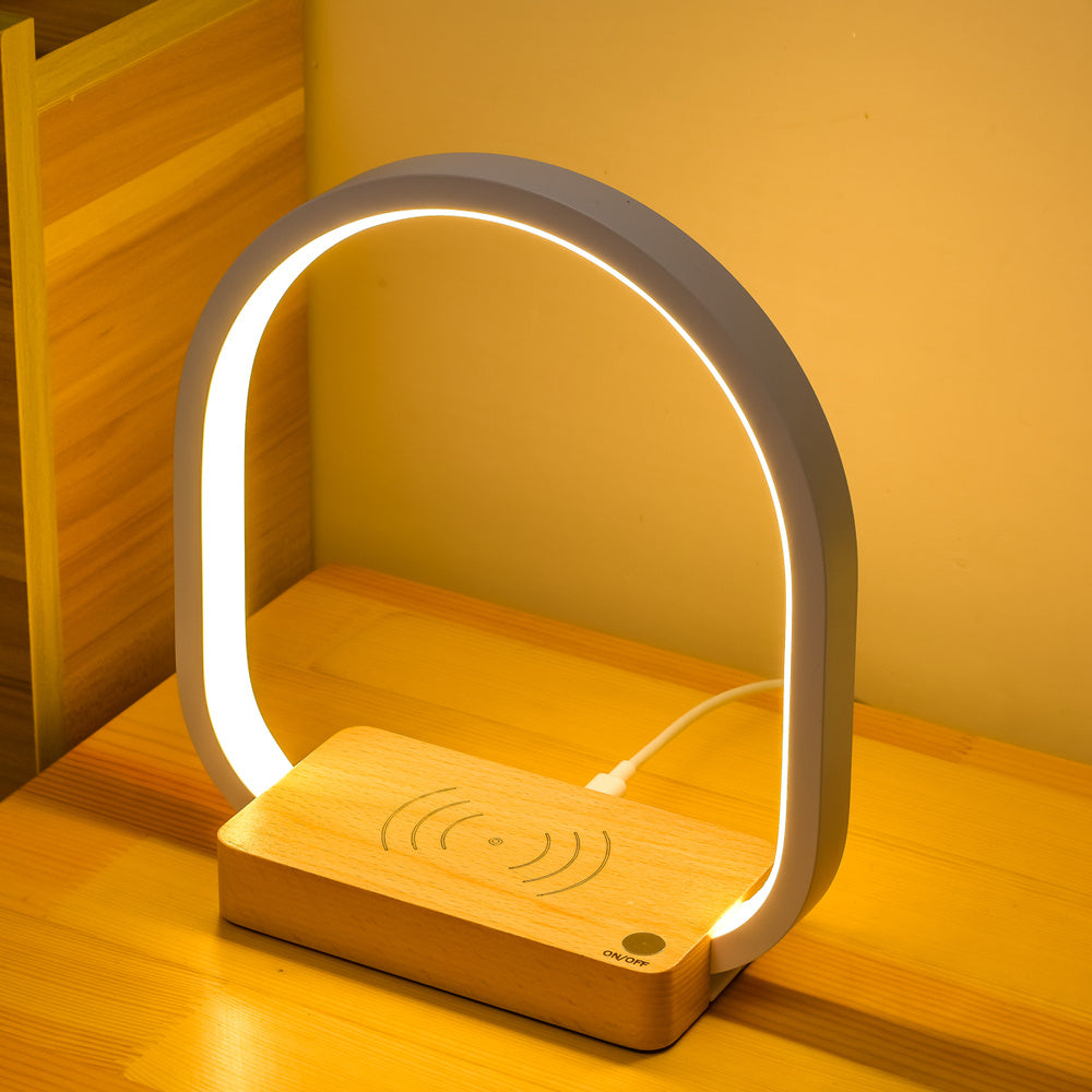 Modern lamp with wooden base and wireless charging pad on a wooden surface.