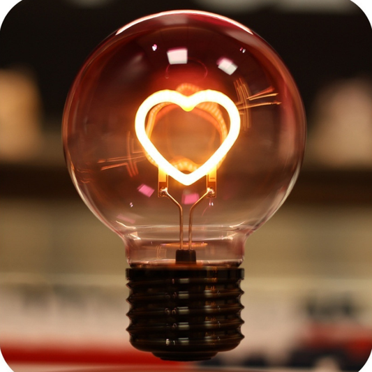Light bulb with a heart-shaped filament on a blurred background