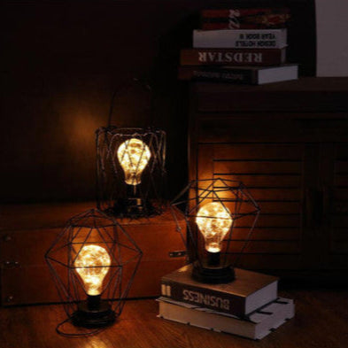 Three vintage-style light bulbs in wire cages on books against a dark background