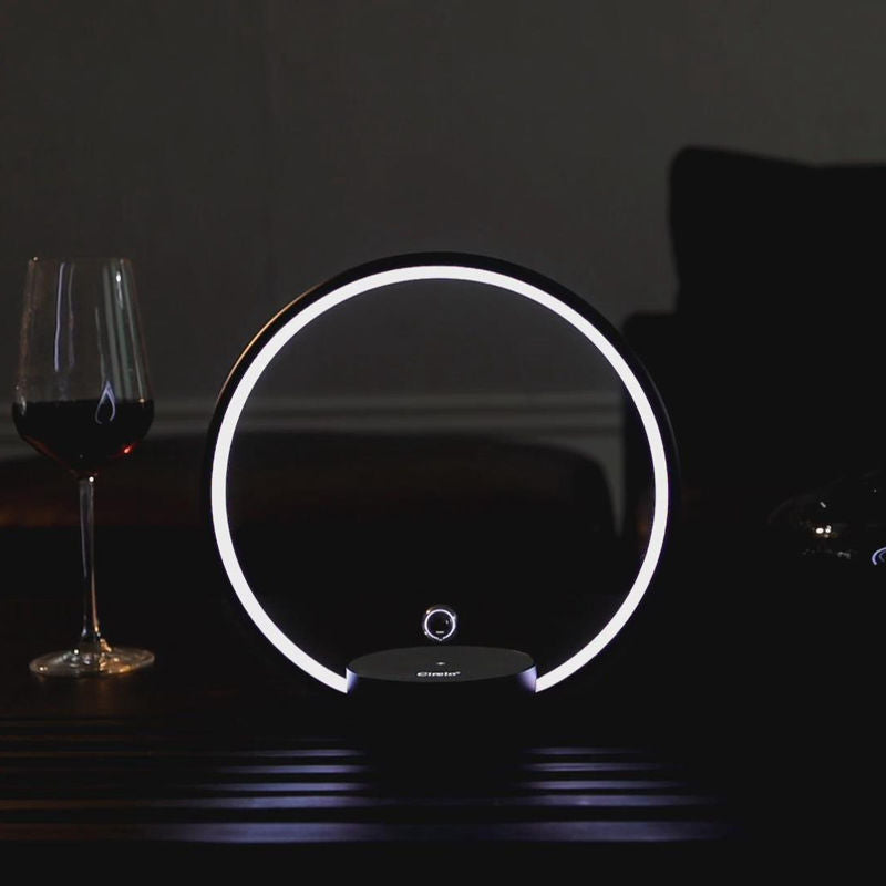 Round light fixture with glowing rim on a dark surface next to a glass of red wine.