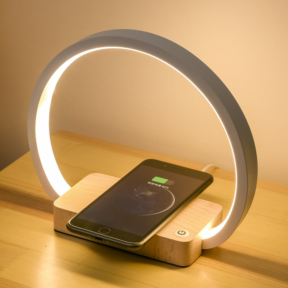Modern charging station with a smartphone on a wooden base, illuminated by a circular light.