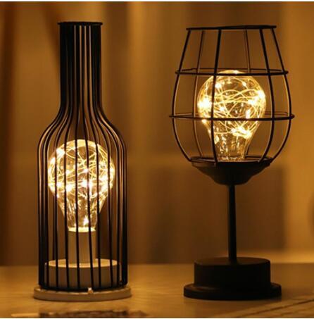 Two decorative lamps with wire bulb lights inside metal cages on a wooden surface.