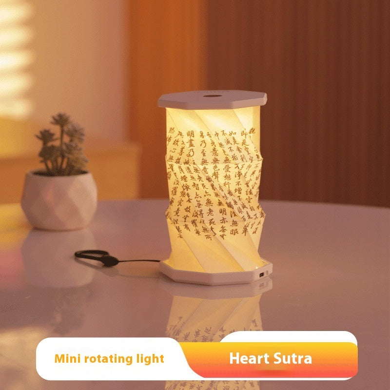 Mini rotating light with 'Heart Sutra' text on a reflective surface with a plant in the background.