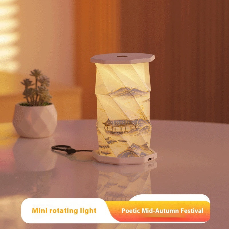 Decorative mini rotating light with scenic design on a table next to a plant