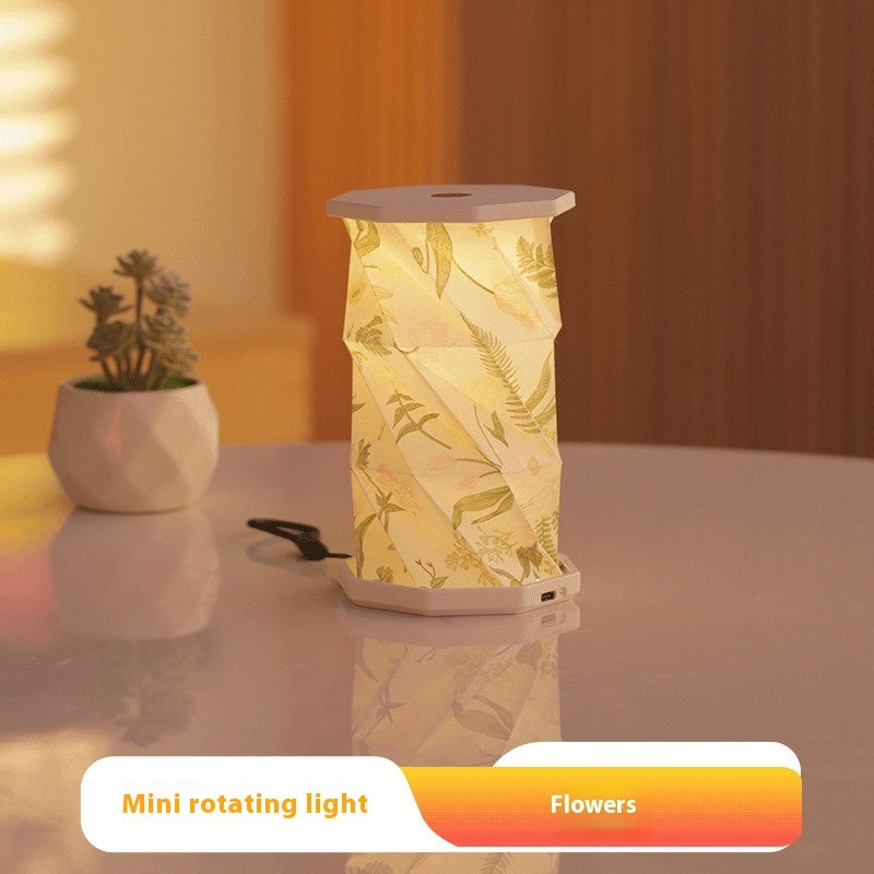 Mini rotating light with floral design on a reflective surface, with a plant in the background.