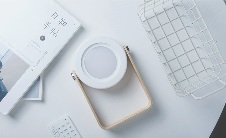 White electronic device on a wooden stand with a white surface and minimal items.