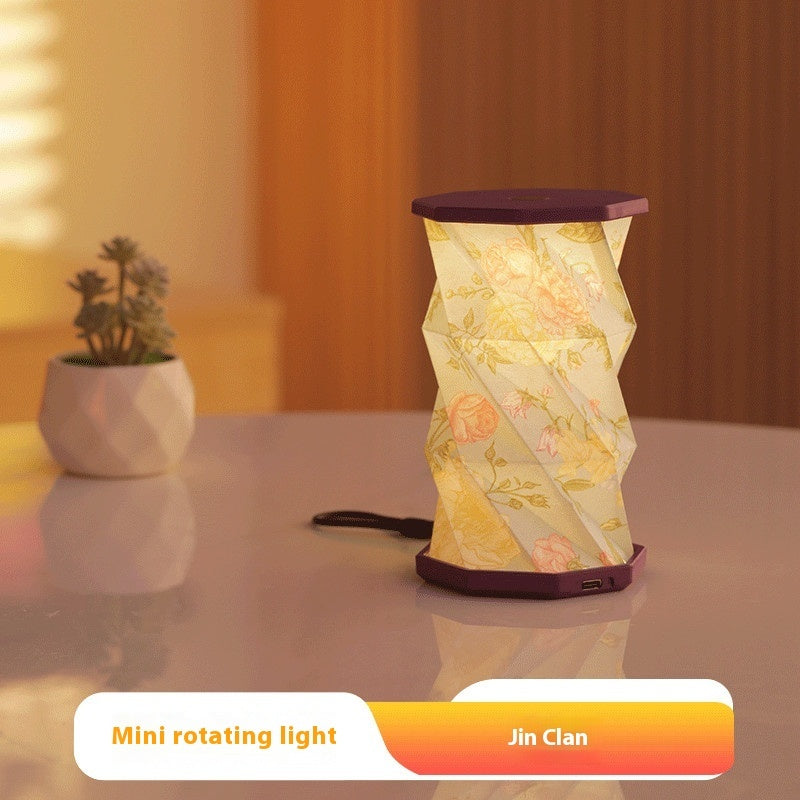Mini rotating light with floral design on a table next to a plant, branded 'Jin Clan'.