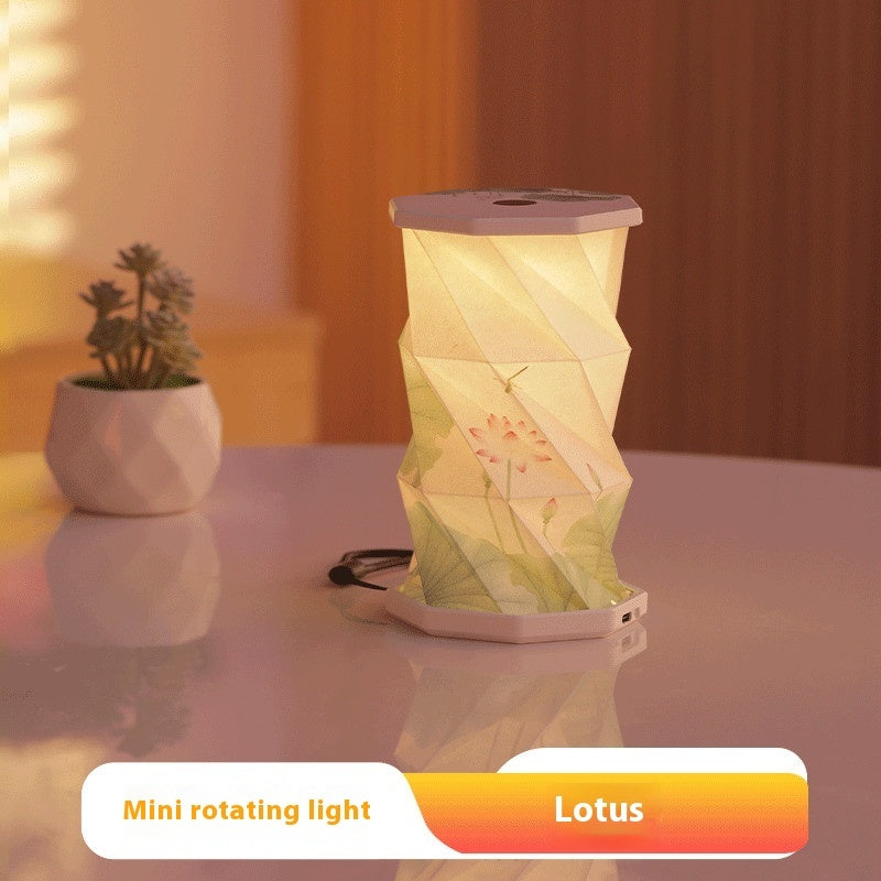 Mini rotating light with 'Lotus' design on a reflective surface with a plant in the background.