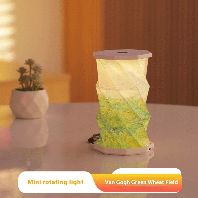 Mini rotating light with Van Gogh Green Wheat Field design on a table with a plant in the background.