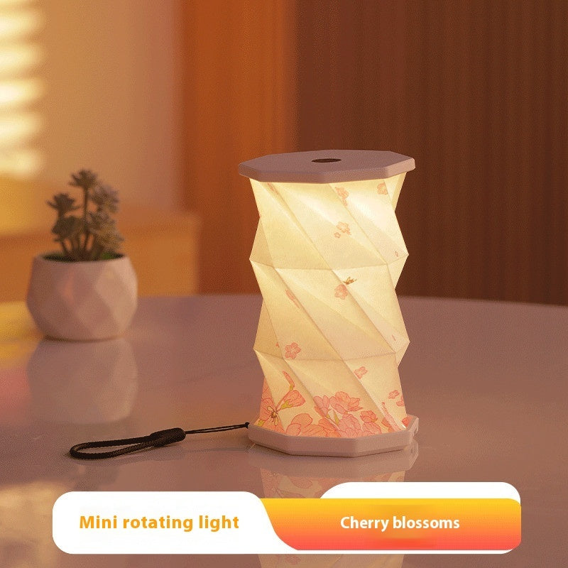 Mini rotating light with cherry blossoms design on a table with a plant in the background