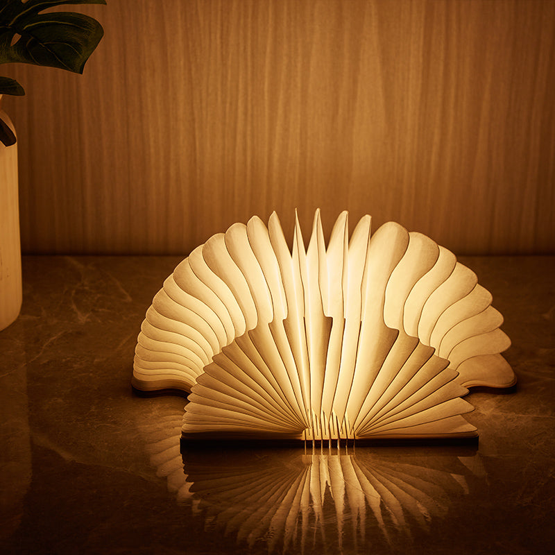 Wooden book-shaped lamp emitting a warm glow on a reflective surface.