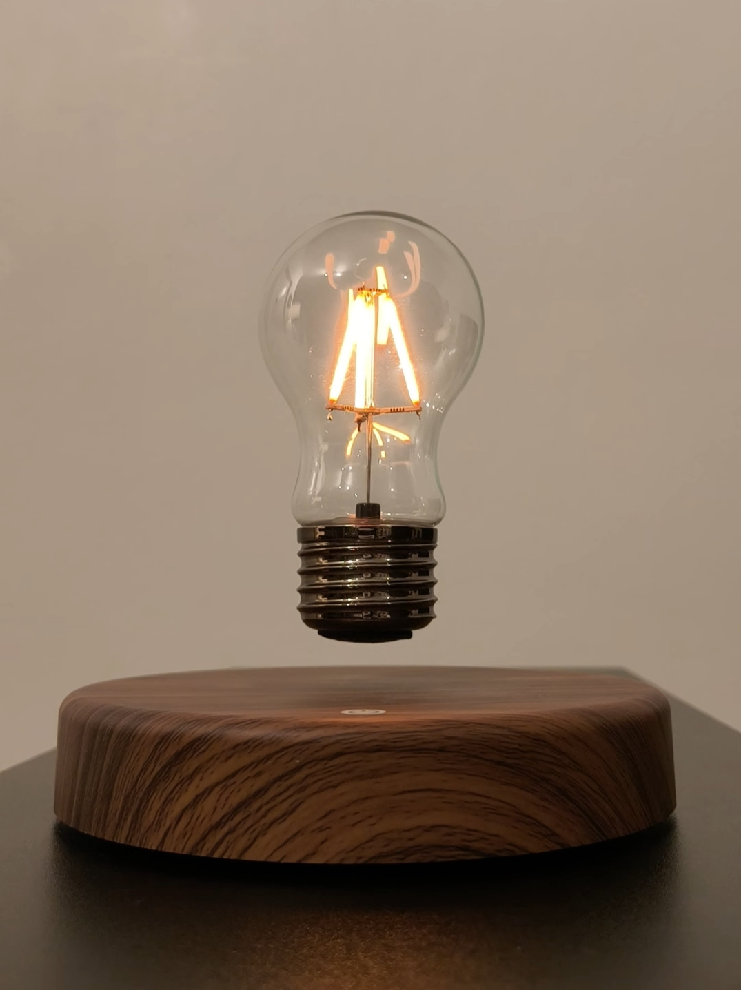 levitating vintage filament light bulb floating over wooden style base