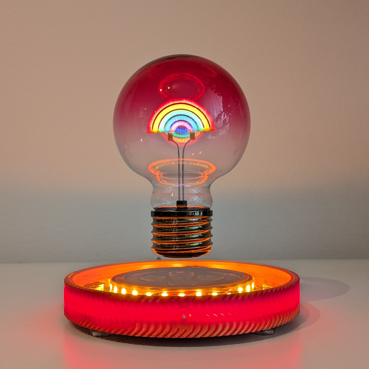 Light bulb with rainbow design on a red base against a neutral background