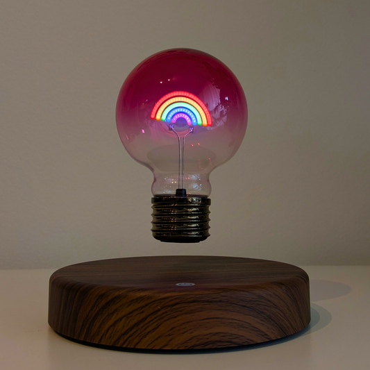Light bulb with rainbow design on a wooden base against a neutral background