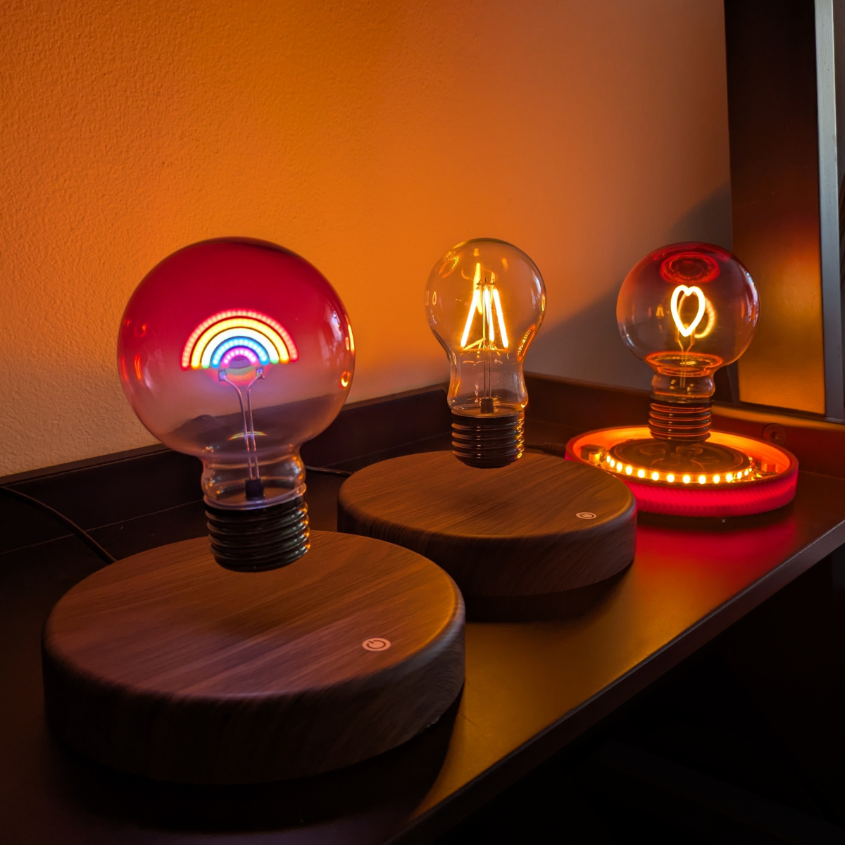 Three light bulb-shaped devices on wooden bases with colorful displays against a warm-toned wall.