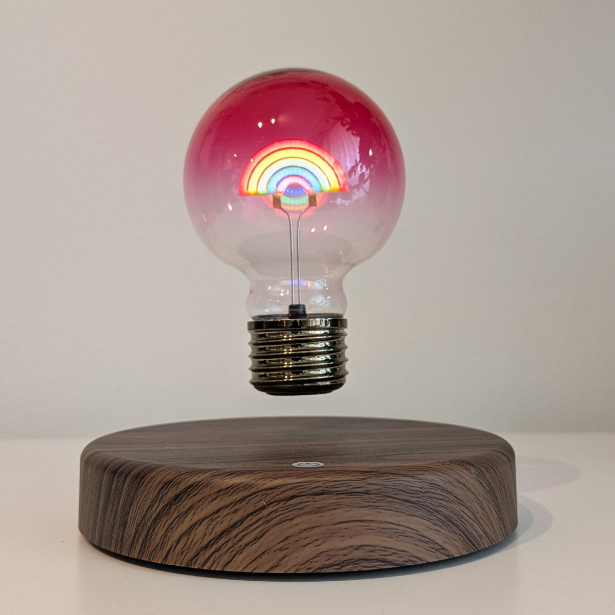 Light bulb with rainbow design on a wooden base against a white background